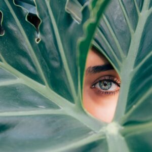 woman peeking over green leaf plant taken at daytime